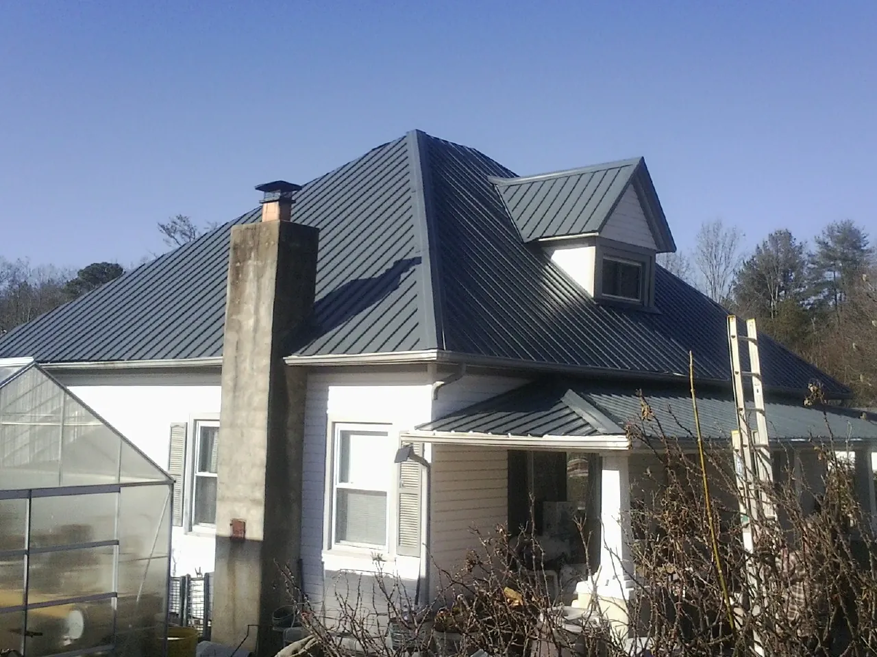 Dark blue standing seam metal roof on a white farmhouse with dormer — Slate & Tile Roof Repair by Roofing Brothers in Pueblo