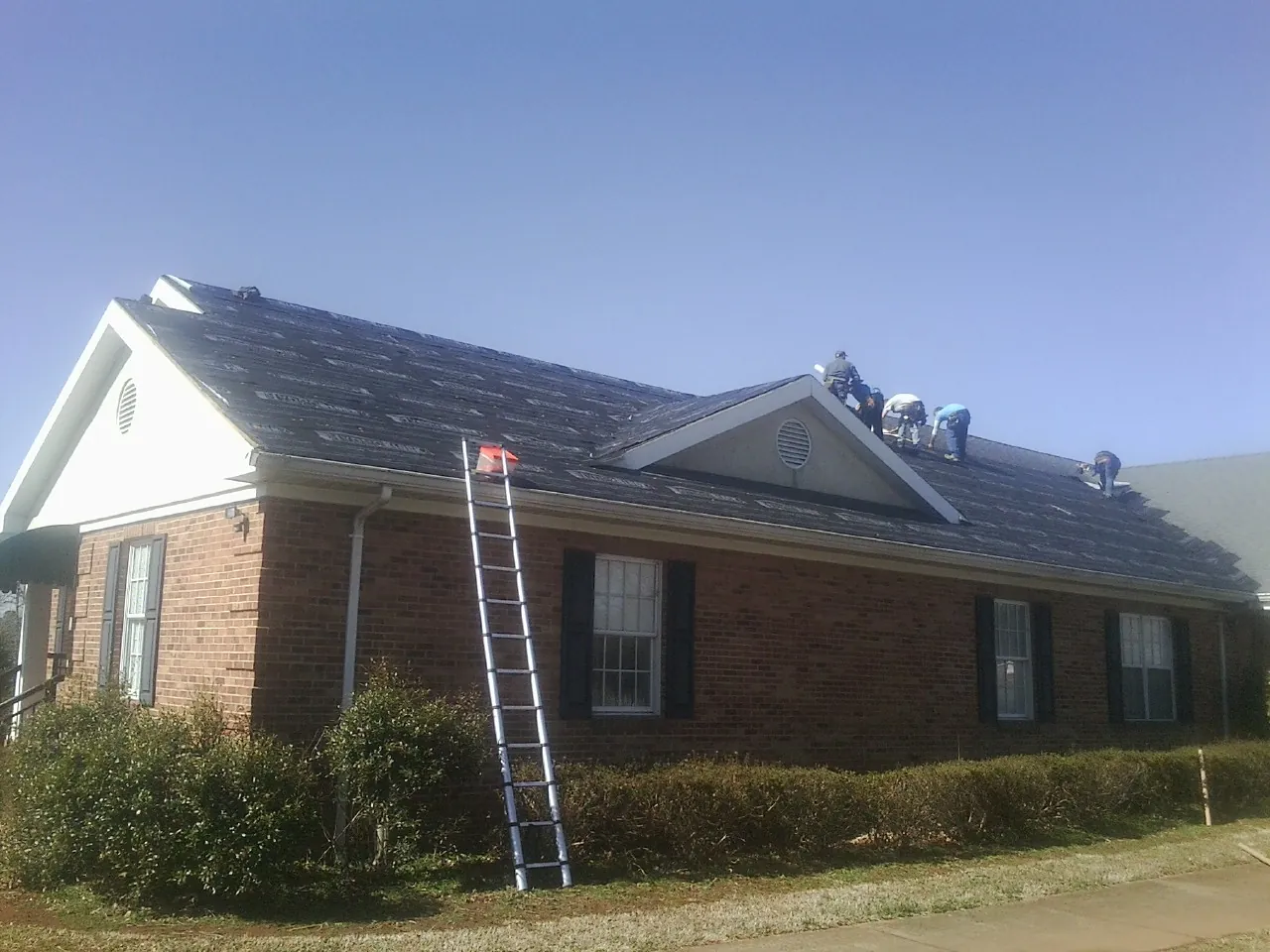Crew tearing shingles off a brick ranch roof with a ladder set — Emergency Roof Repair work by our crew in Pueblo