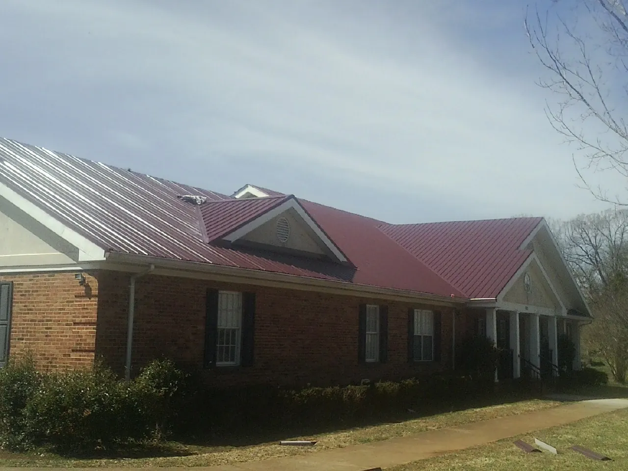 Red metal roof with gabled entries on a long brick building, from a Hail Damage Roof Repair job in Pueblo
