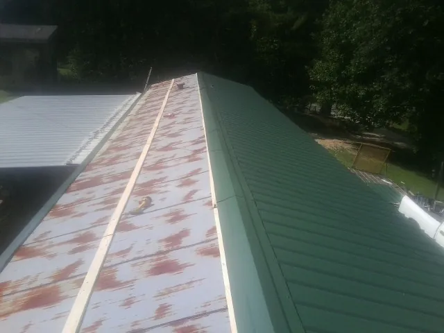 Old rusted panels beside newly installed green metal roofing — Wind Damage Roof Repair by Roofing Brothers in Pueblo