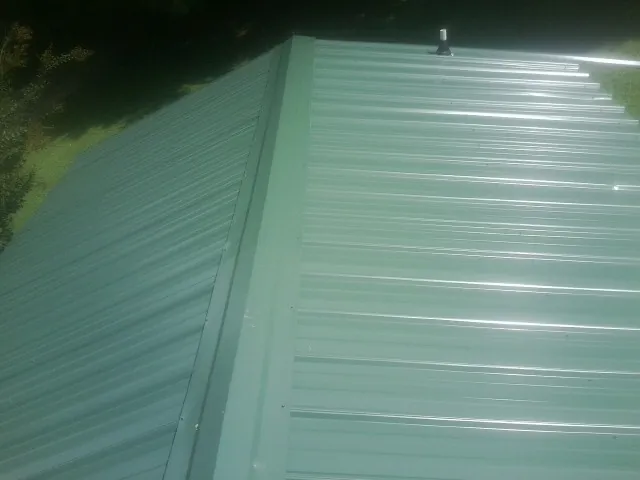 New green metal panels meeting at the ridge of a roof — Flat Roof Repair work by our crew in Pueblo