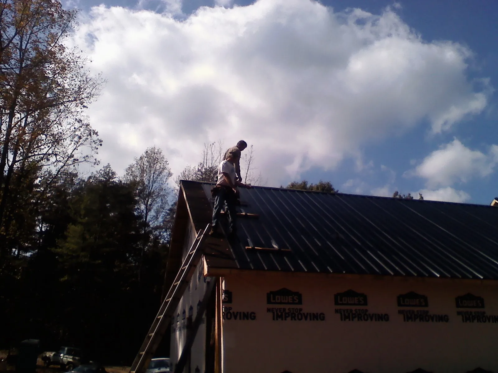 Roofer fastening dark metal panels high against a cloudy sky, from a Roof Inspection job in Pueblo