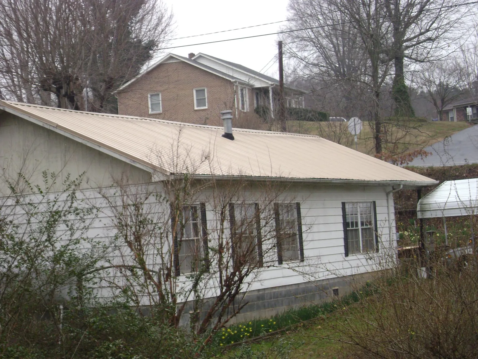 Tan metal roof on a white sided house set into a hillside — Commercial Roofing by Roofing Brothers in Pueblo